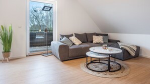 Een moderne woonkamer met een grijze bank, een ronde salontafel en een grote schuifglazen deur die uitkomt op een balkon.