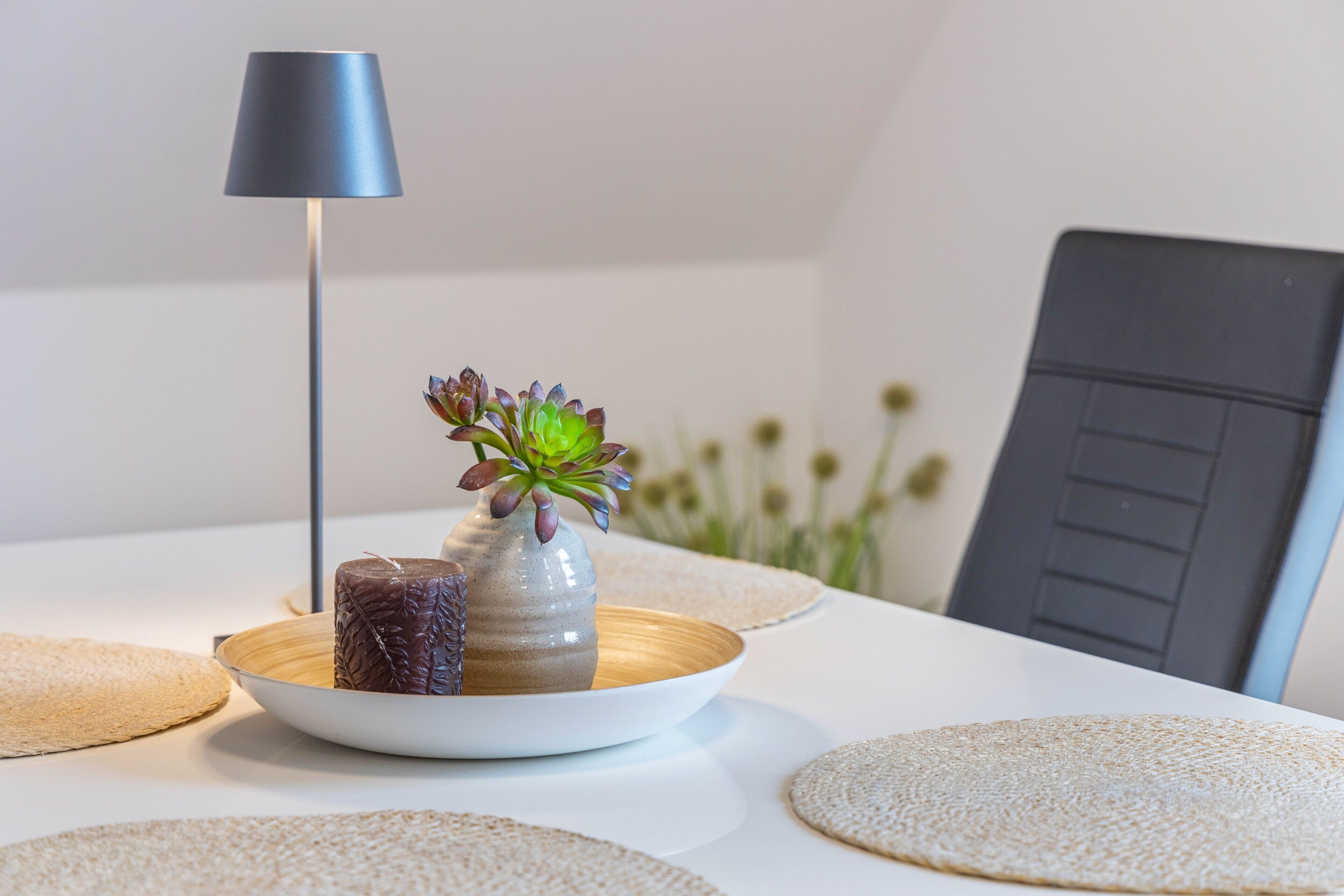 A table with a vase of succulents, a candle, and a lamp.