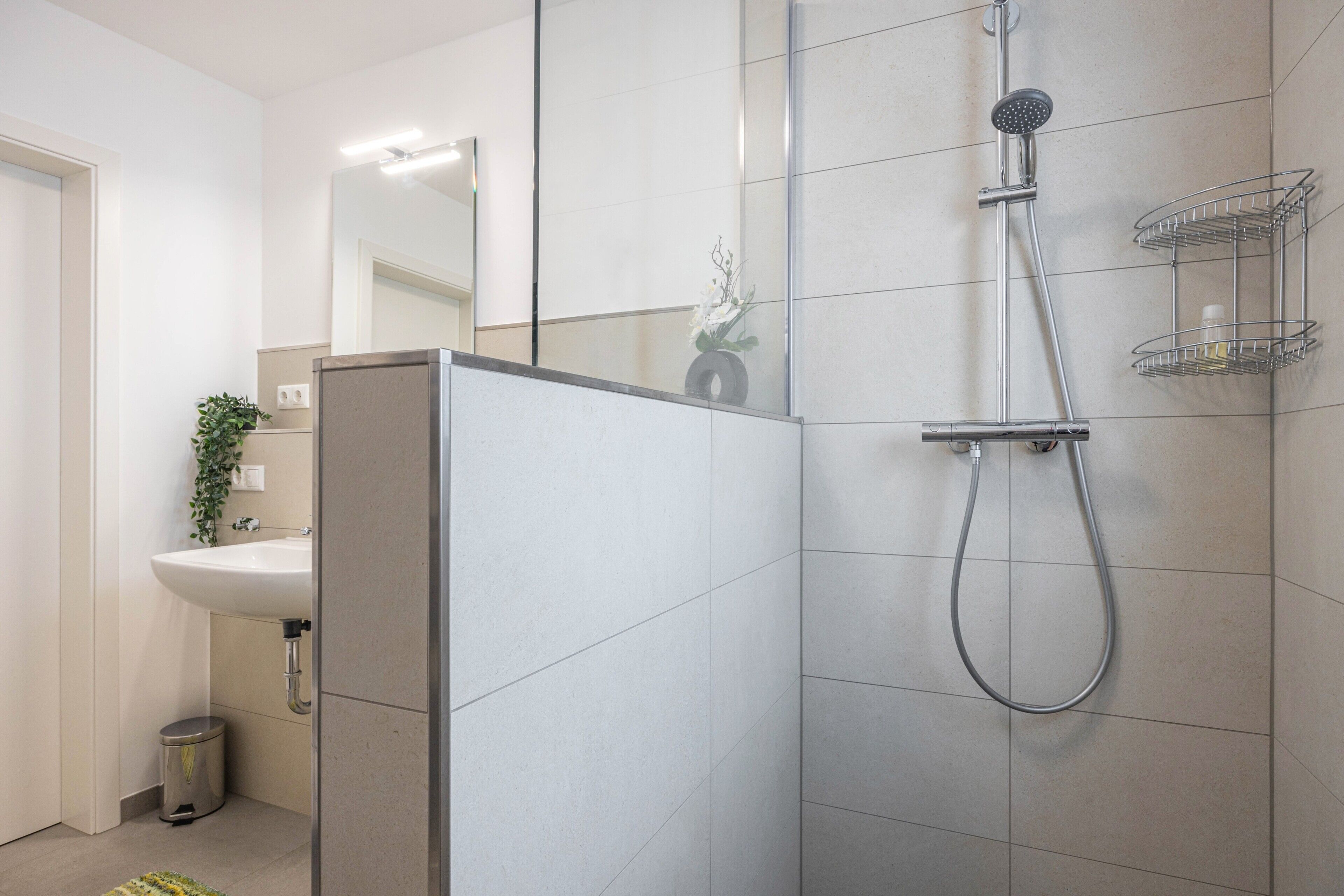 Une salle de bain moderne équipée d’une douche, d’un lavabo et d’un miroir.
