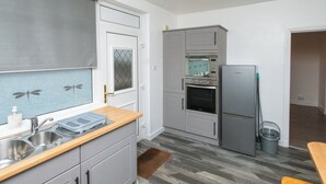 Eine kleine Küche mit grauen Schränken, einem eingebauten Ofen, einer Mikrowelle und einem Kühlschrank.