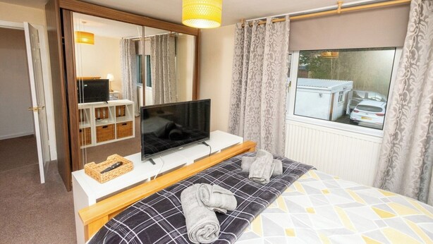 Ein Hotelzimmer mit Bett, Fernseher, Spiegel, Fenster mit Vorhängen und Blick auf ein Auto draußen.