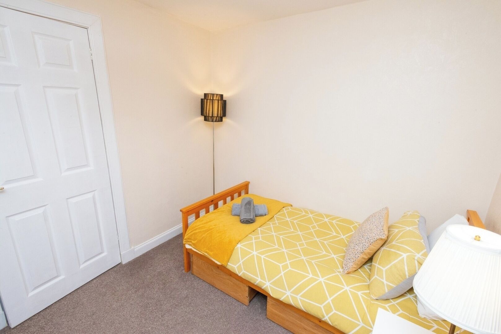 Une petite chambre à coucher, bien rangée, avec un lit simple, une table de chevet et une lampe fixée au mur.