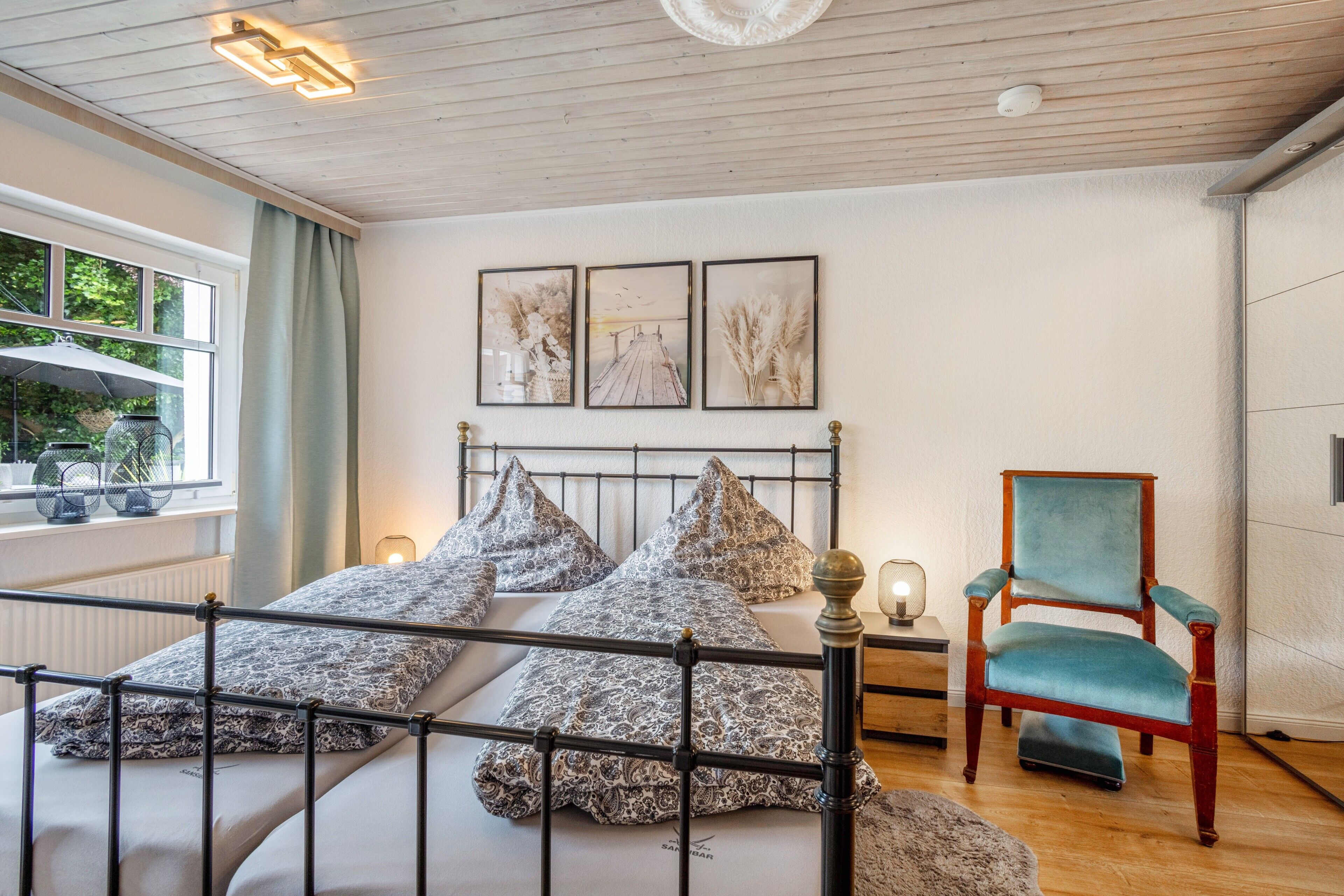 A bedroom with a bed, a chair, a window, and wall art.