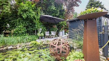 A garden with a pond, a metal sculpture, and a seating area with chairs and an umbrella.