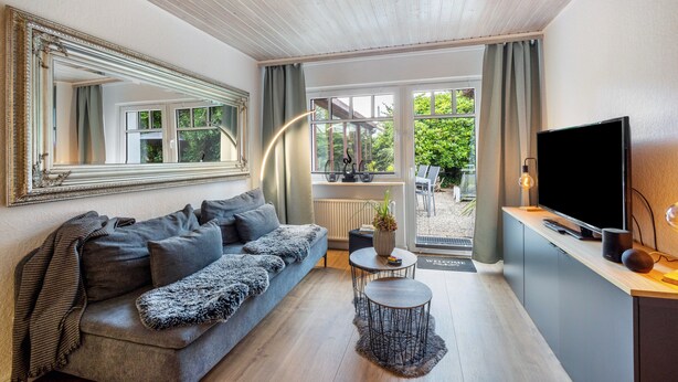 Un salon moderne avec un canapé, une table basse, un téléviseur et une grande fenêtre avec des rideaux.