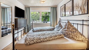 Une chambre à coucher avec un lit, une télévision, une fenêtre et des œuvres d’art encadrées accrochées au mur.