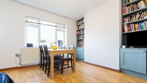 A dining area with a wooden table and chairs, a bookshelf, and a radiator. - 2 bedroom flat in Hackney, London. Next to several stations and restaurants (London)