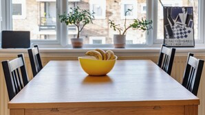 A dining table with a yellow bowl, surrounded by black chairs, in a room with large windows and potted plants. - 2 bedroom flat in Hackney, London. Next to several stations and restaurants (London)