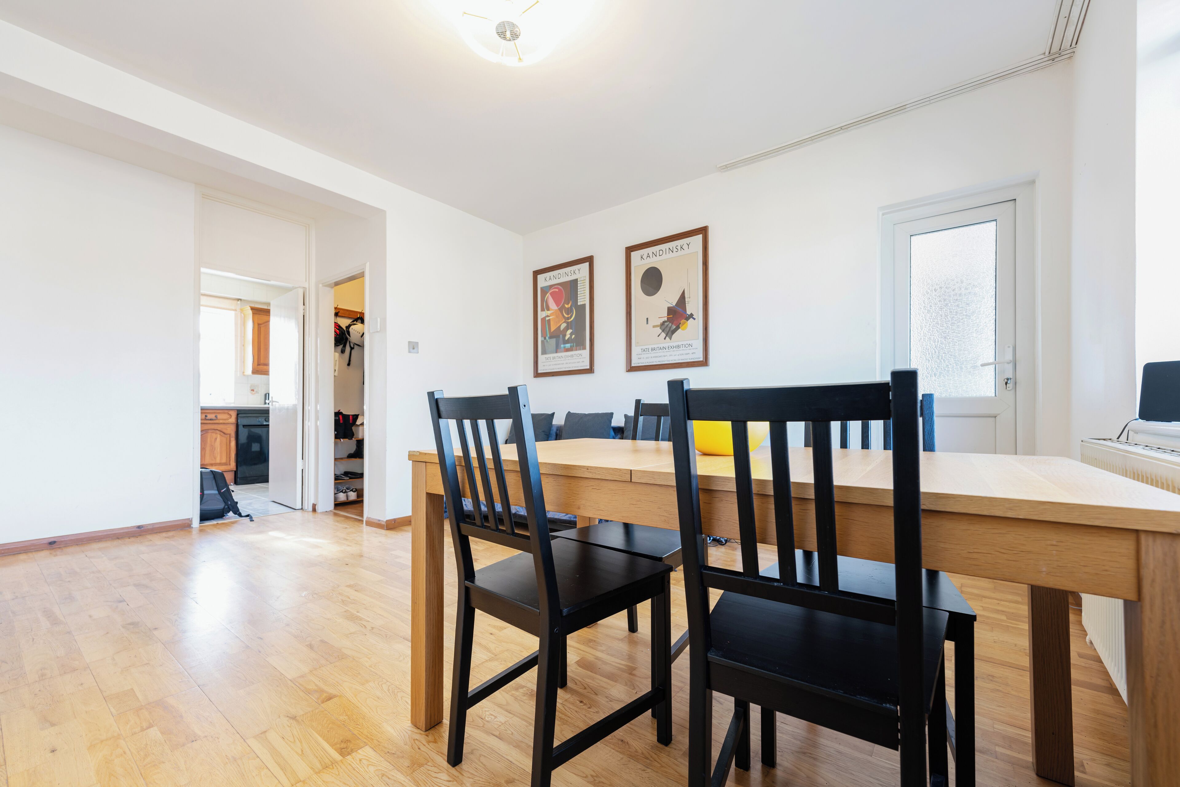 Uma sala de jantar com uma mesa de madeira e cadeiras pretas, duas molduras na parede e uma porta que dá para outro cômodo.