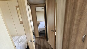 A narrow hallway with wooden doors leading to a bedroom with a bed and a bathroom. - Ty Mawr Chalet Sleeps 6 with Fireplace (Abergele)