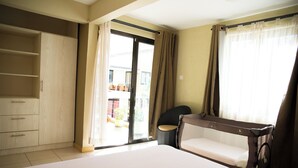 Een hotelkamer met een groot bed, een kledingkast, een zithoekje en een balkon met plantenpotten.