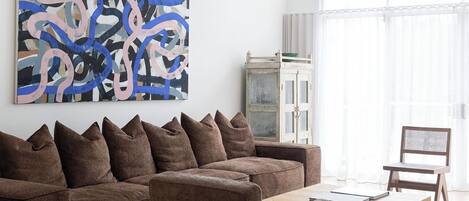 A modern living room with a brown sofa, a wooden coffee table, and a large abstract painting on the wall.