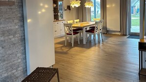 Moderni keittiö, jossa on ruokailutila, puinen portaikko ja suuret ikkunat.