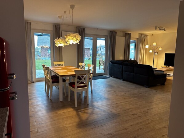 A modern living room with a dining area, large windows, and a flat-screen TV.