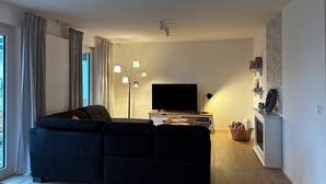 Moderni olohuone, jossa on kulmasohva, taulutelevisio, lattiavalaisin ja takka.
