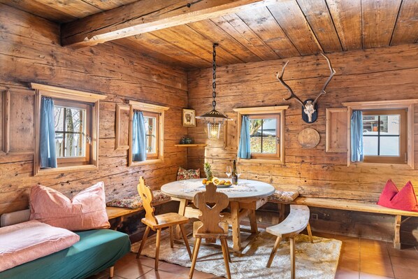 A wooden cabin interior with a round dining table, wooden benches, and a cozy seating area.