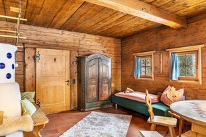 A wooden cabin interior with a bed, a wooden cabinet, a dining table, and a large window.