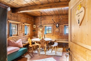 A wooden cabin interior with a round dining table, wooden benches, a sofa, and a wall-mounted deer head.
