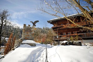 Eine Holzhütte mit Steinmauern, verschneitem Gelände und einer Adlerstatue.