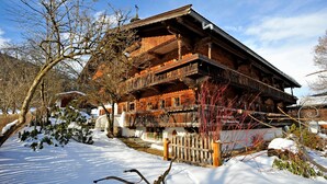 A wooden chalet with a balcony, surrounded by snow and trees. - Apartment '02 Mühlfeldhof A3' with Mountain View, Shared Terrace and Wi-Fi (Kelchsau)