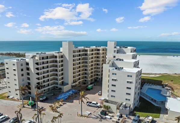 A multi-story hotel with a pool, located near a beach with clear skies.
