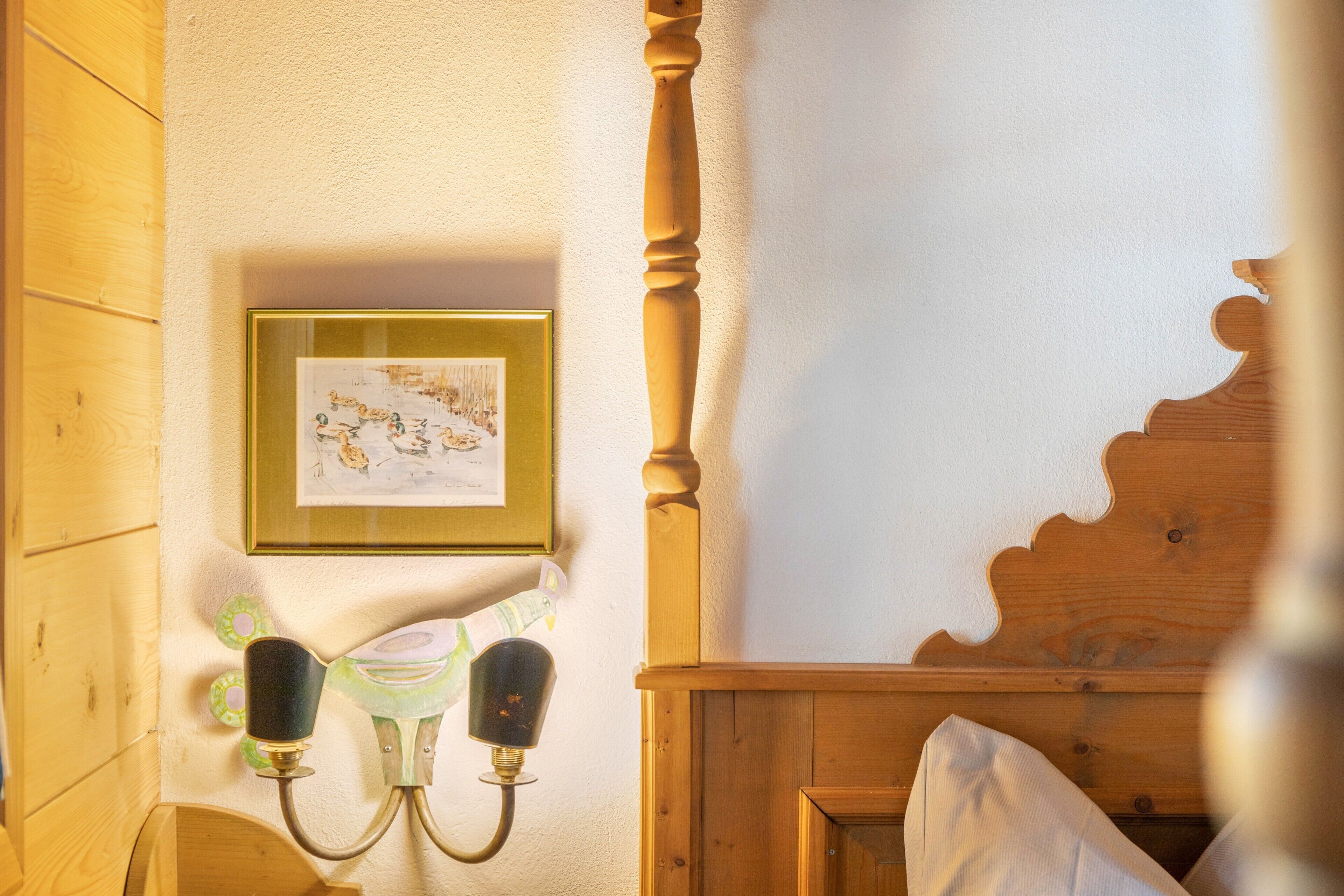 Un lit en bois avec une tête de lit, un cadre photo fixé au mur et un luminaire fixé au mur.