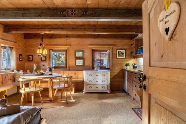 Een houten chaletinterieur met een eethoek, een witte ladenkast en een hartvormig bord aan de muur.