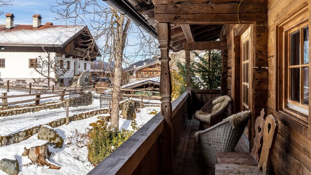 Une cabane en bois dotée d’un porche, de murs en pierre et offrant une vue sur un village enneigé.