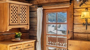 Ein Holzhütten-Interieur mit Fenster, einem Schrank mit Gitterwerk, einer Lampe und einer Wanddekoration.