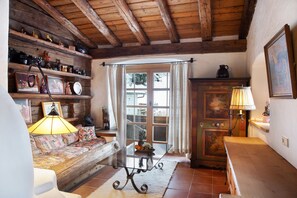 A rustic room with a wooden ceiling, a sofa with a patterned cover, a glass-top table, and a wooden cabinet.