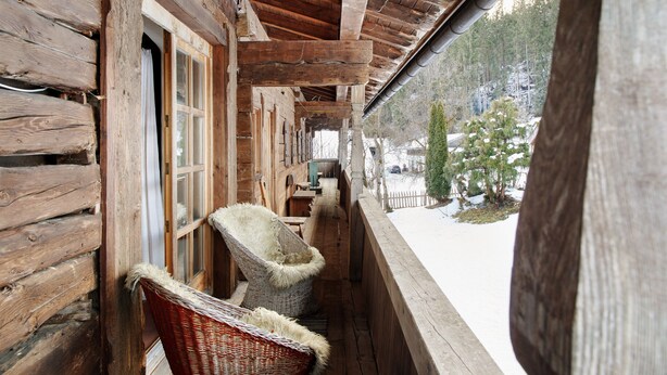 Une cabane en bois dotée d’une véranda, de chaises en osier et offrant une vue sur un paysage enneigé.