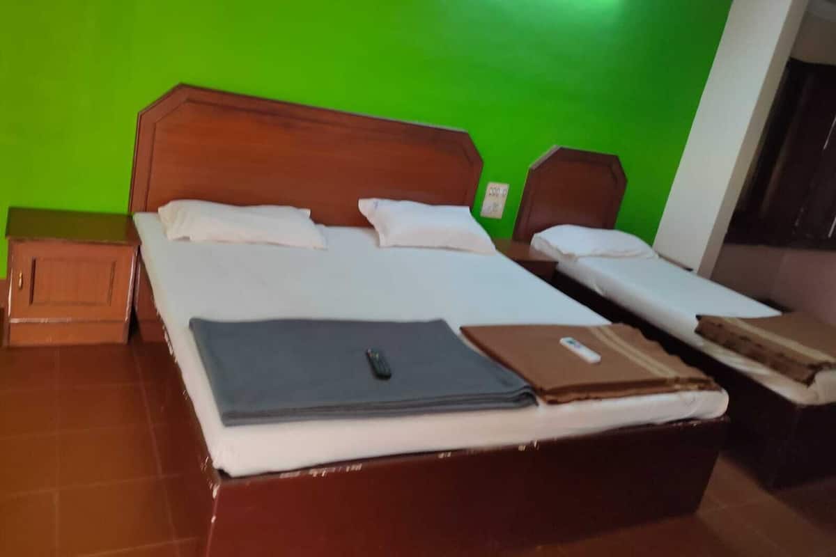 A hotel room with a large bed, two smaller beds, wooden headboards, and a green wall.