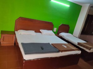 A hotel room with a large bed, two smaller beds, wooden headboards, and a green wall. - Anjana Hotels (Theni)