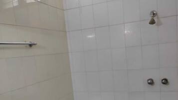 Une salle de bain équipée de toilettes, d’une barre d’appui, d’une poubelle verte et d’une fenêtre avec des stores.