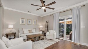 Un salon comprenant un ensemble de canapés, une table basse et un ventilateur de plafond. Une porte-fenêtre coulissante donne accès à un espace extérieur.