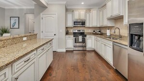 Une cuisine moderne avec des meubles blancs, des comptoirs en granit, des appareils en acier inoxydable et un plancher en bois franc.
