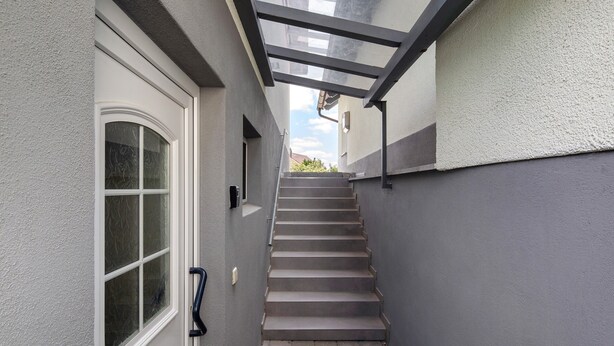 Una escalera estrecha que conduce a una puerta con paneles de vidrio esmerilado, una barandilla de metal y una pared gris.