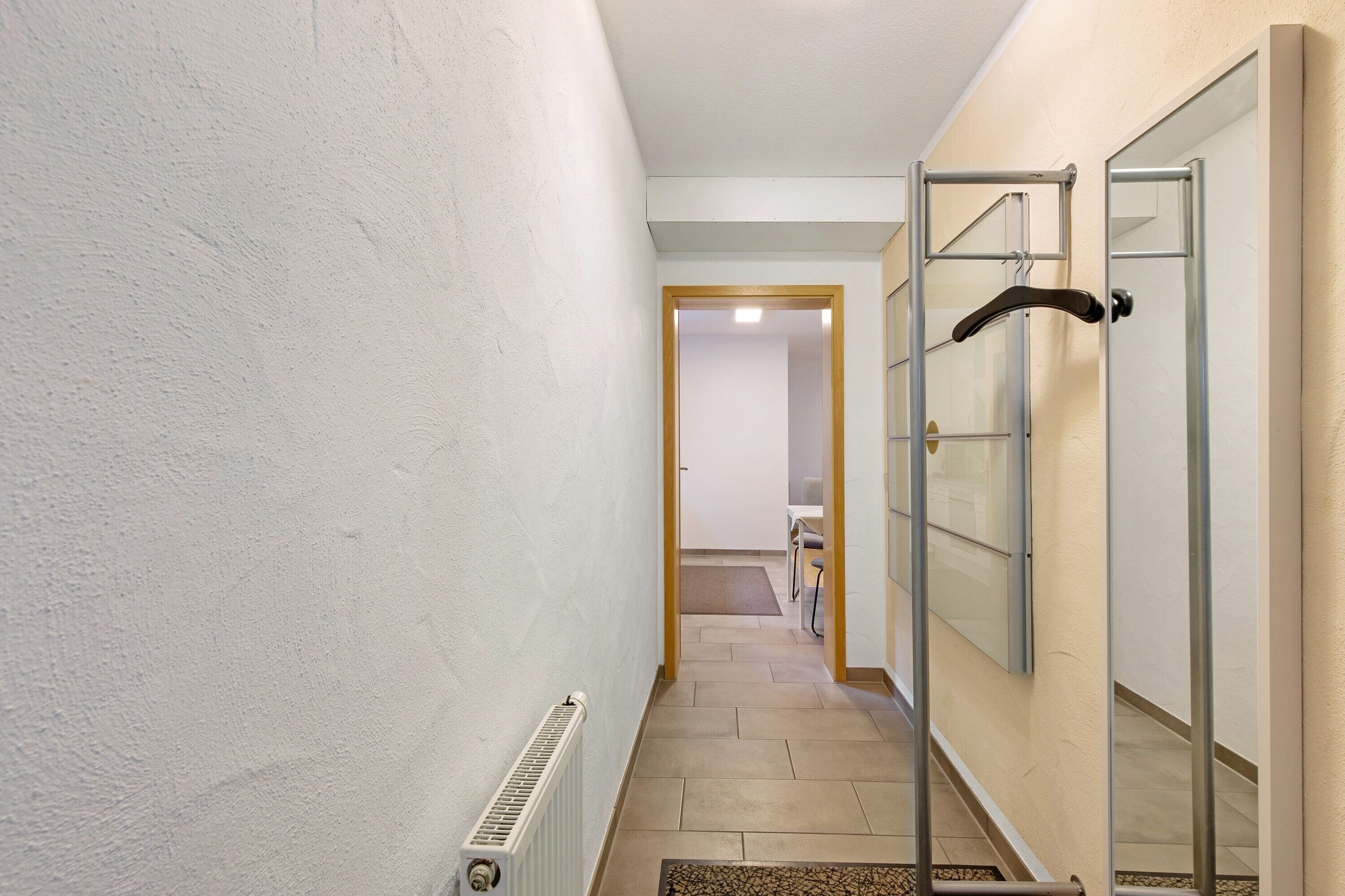 Un passadís amb un radiador, un espai de dutxa amb envidriall i una porta que dona a una altra habitació.