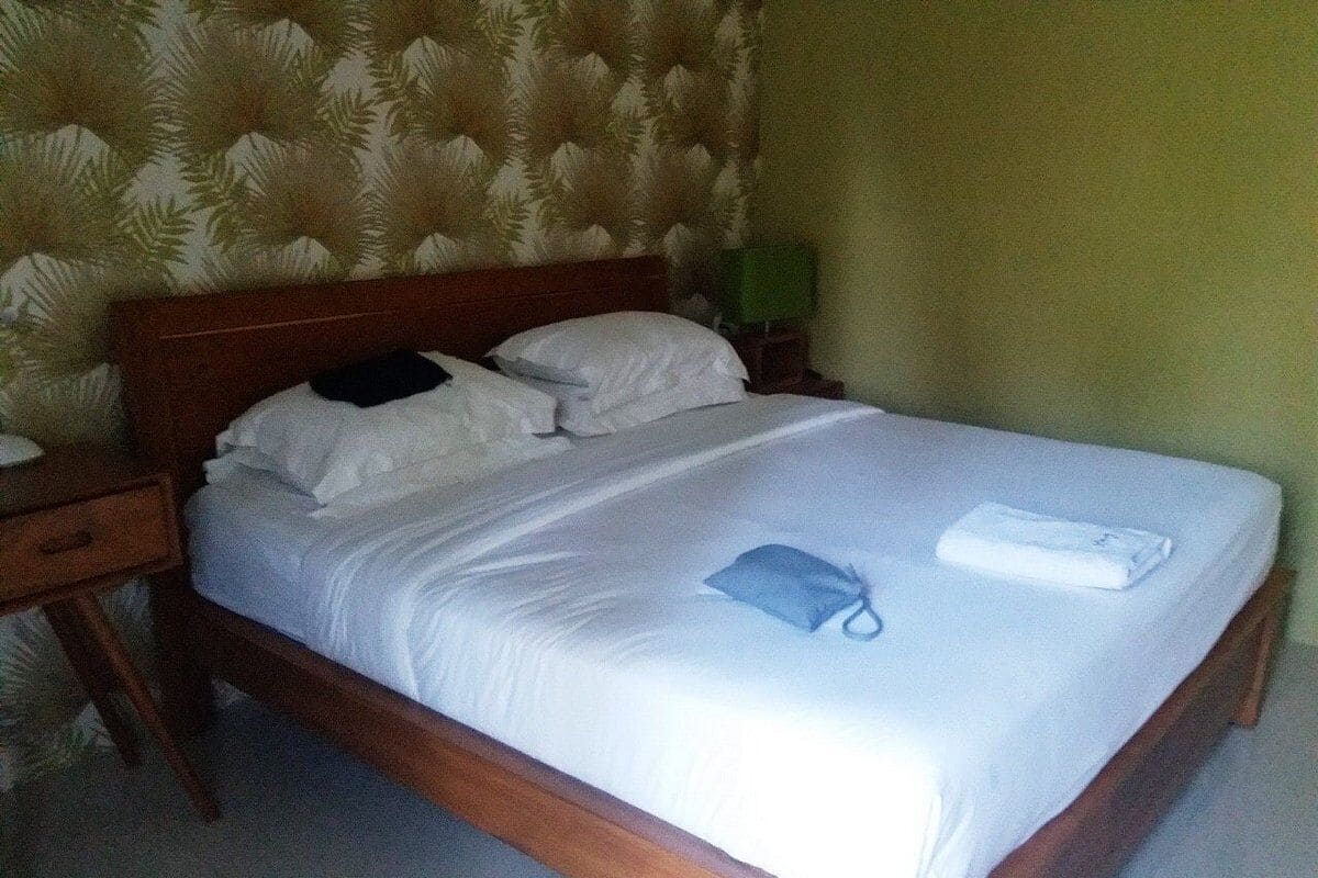 A neatly made bed with white linens, a blue towel, and a folded white towel on a wooden bed frame.