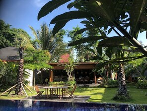 Ein tropisches Resort mit Pool, Essbereich im Freien und üppiger Vegetation.