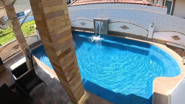 A swimming pool with a waterfall feature, surrounded by a stone wall and a tiled deck. - Beautiful pool villa 200 meters from the beach and the beach promenade 4 bedrooms (Bang Saray)