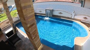 A swimming pool with a waterfall feature, surrounded by a stone wall and a tiled deck. - Beautiful pool villa 200 meters from the beach and the beach promenade 4 bedrooms (Bang Saray)