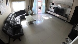 A living room with a black leather sofa, a glass coffee table, a flat-screen TV, and a sliding glass door leading to a patio. - Beautiful pool villa 200 meters from the beach and the beach promenade 4 bedrooms (Bang Saray)