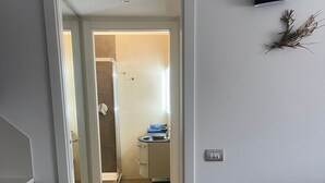 Un couloir menant à une salle de bain équipée d’une douche, d’un lavabo et d’un porte-serviettes.