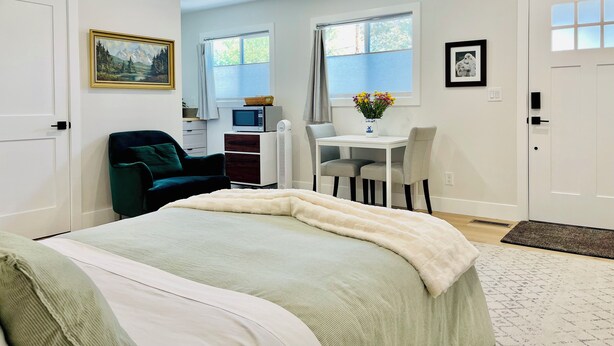 A bedroom with a bed, a desk, and a chair. There is a window with curtains, a picture on the wall, and a door.
