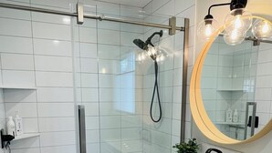 A modern bathroom with a glass-enclosed shower, a white sink, and a mirror with a round frame.