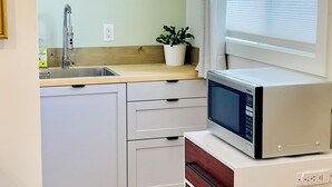 A compact kitchen with a built-in microwave, a sink, and a window with blinds.