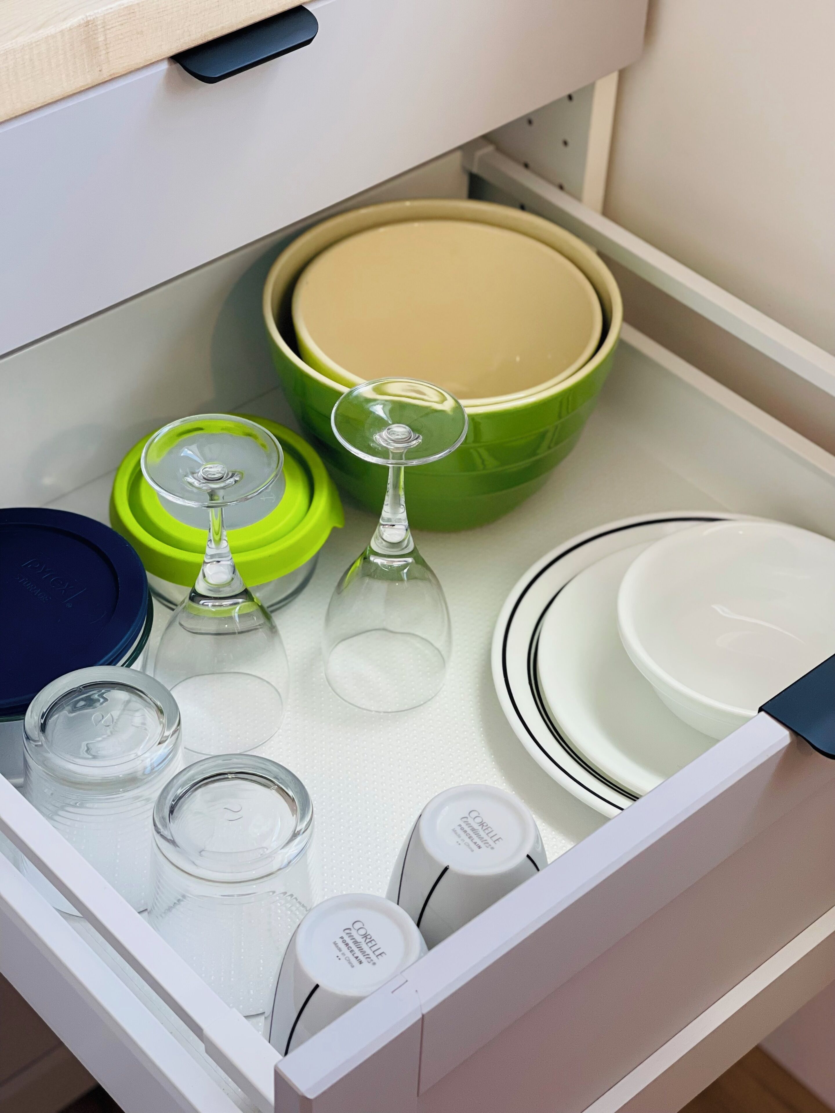 A kitchen drawer containing various items including a green bowl, a wine glass, and several containers.