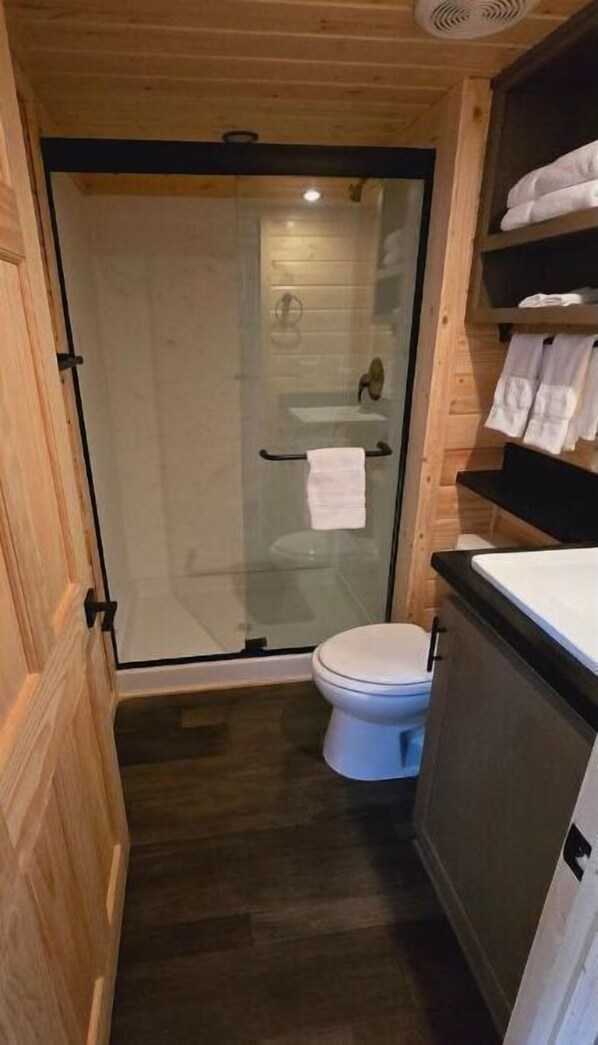 A small bathroom with a glass shower door, a toilet, and a sink with a towel rack above it.
