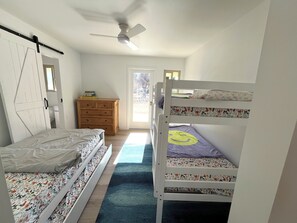 Une chambre avec un lit superposé, une commode, un ventilateur de plafond et une porte donnant sur un balcon.